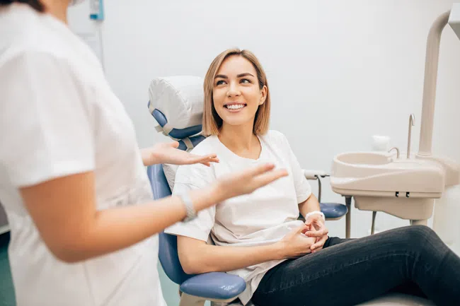 Smiling woman in dental chair talking to dental professional in modern clinic setting.