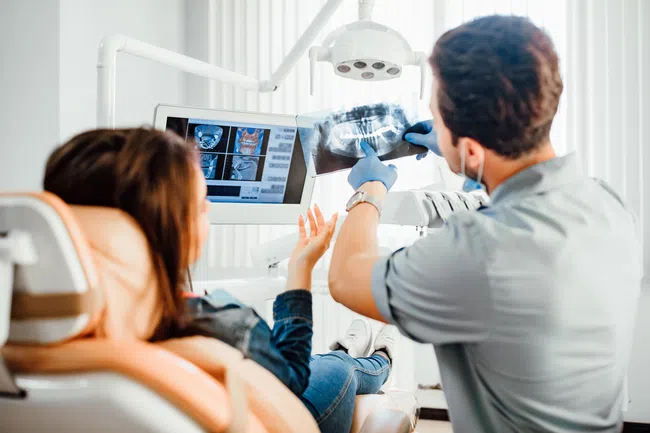 Dentist showing a dental x-ray to a female patient in a modern dental clinic with digital screens.