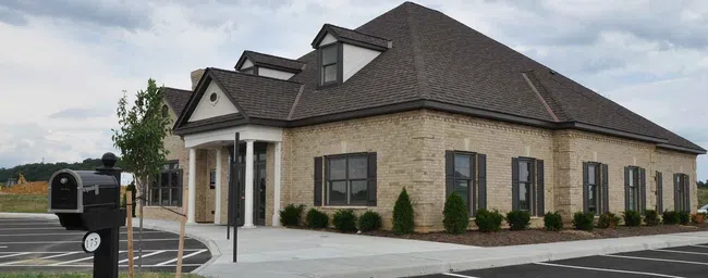 Modern single-story brick office building with a dark roof, surrounded by parking and landscaping under cloudy sky
