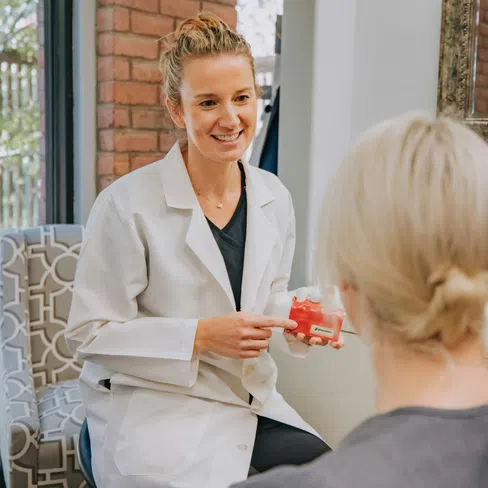 Dentist explaining dental implant model to patient in a bright modern office during consultation.