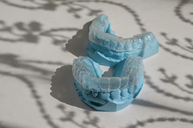 Transparent dental aligners on blue dental molds placed on a white surface with soft shadows.
