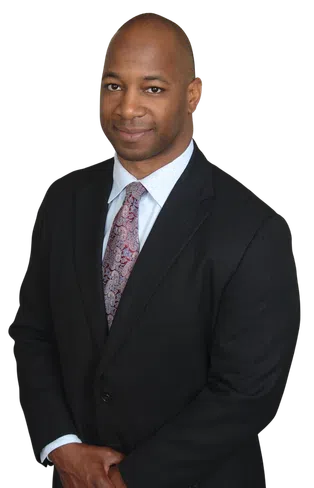 Confident African American man in a dark suit and patterned tie smiling with hands clasped in front