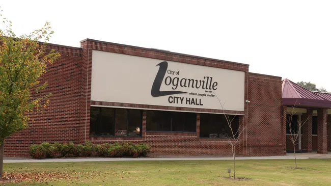 Brick Loganville City Hall building with large sign and surrounding grass and trees under cloudy sky