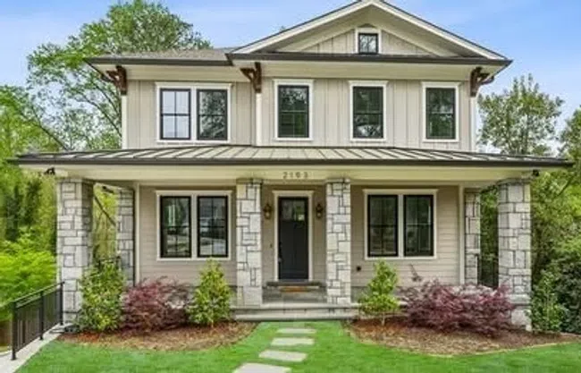 Two-story modern farmhouse with stone pillars, large windows, and a manicured front lawn with stepping stones.