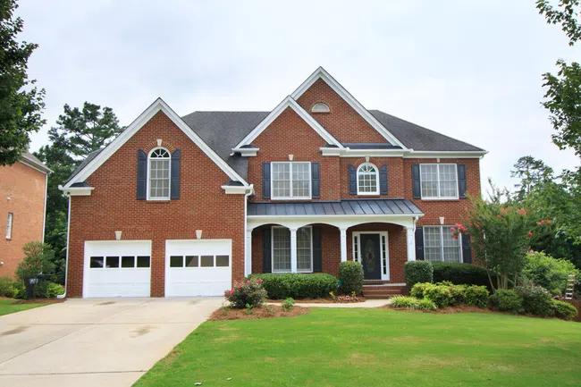 Large two-story brick house with white trim, arched windows, double garage, and well-kept front yard with green lawn.