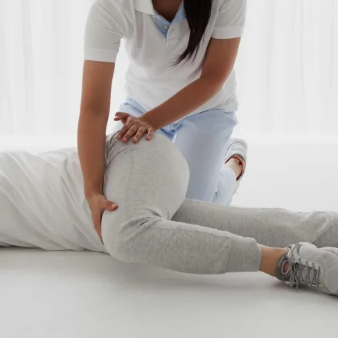 Physical therapist assisting a person with leg stretch exercise on floor in bright room