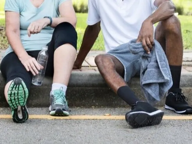 Group of diverse runners sitting on curb resting after workout, showing athletic shoes and casual sportswear.
