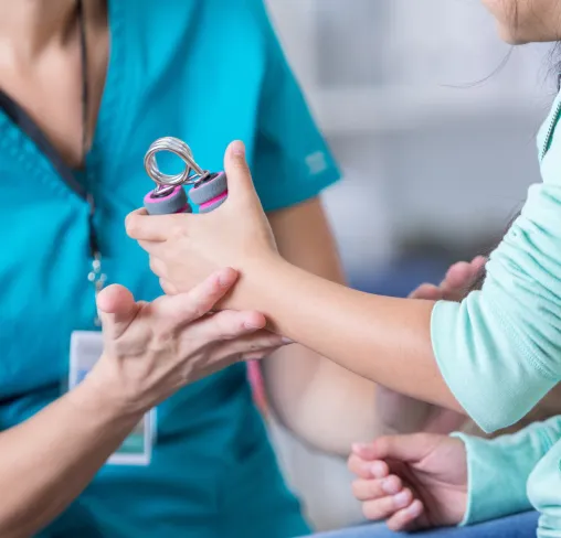 Therapist guiding child's hand exercising with a hand grip strengthener during rehabilitation therapy session.