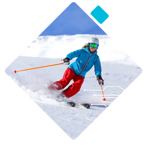 Skier in blue jacket and red pants skiing down snowy slope with mountains and clear blue sky in background.