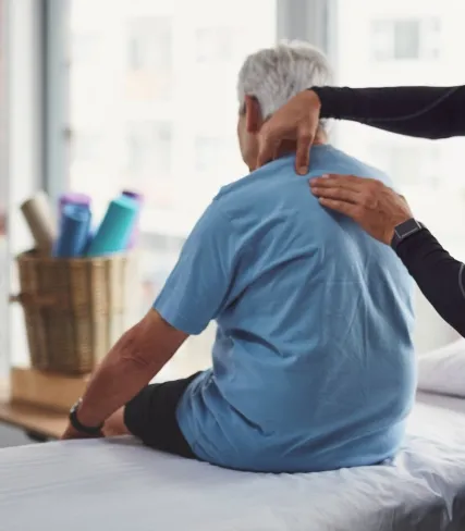 Senior man receiving shoulder massage or physical therapy in a bright room with yoga mats in the background