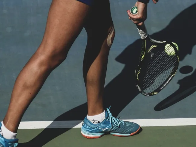 Tennis player hitting a ball on a blue hard court with racket and wearing blue sneakers