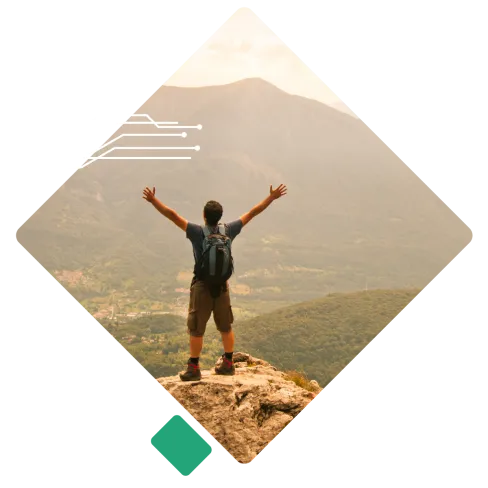 Hiker with backpack raising arms on rocky cliff overlooking a vast mountainous valley in daylight