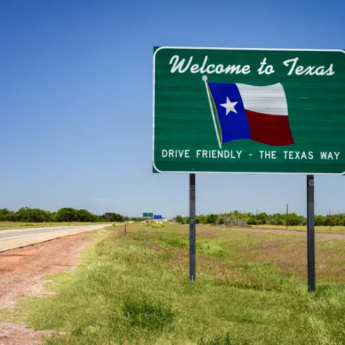 Welcome to Texas sign featuring the Texas flag against a clear blue sky.