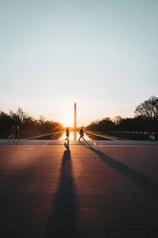 Silhouettes of people walking by the Washington Monument at sunset, reflecting on the water.