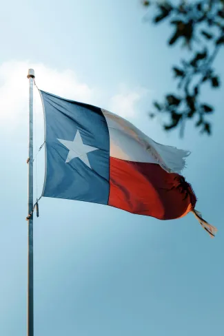 The Texas flag waving against a bright blue sky with a few scattered clouds.