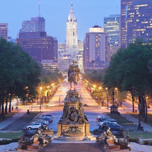 View of Philadelphia's City Hall and statue at dusk with city lights glowing on a serene street.