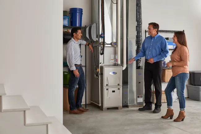 HVAC technician explaining furnace system to a couple in a modern home basement with organized storage