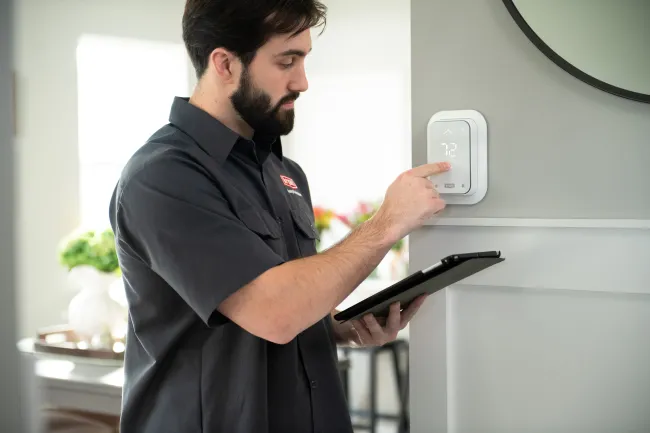 Technician adjusting a smart thermostat set to 72 degrees in a modern home while holding a tablet.