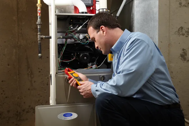 Technician inspecting a furnace with a digital multimeter in a basement setting.