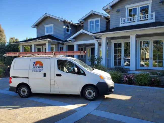 White Total Home Environmental service van parked in front of a modern two-story gray house with large windows.