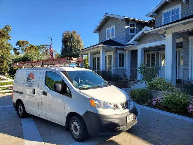 White service van with ladder on roof parked outside modern two-story house on sunny day