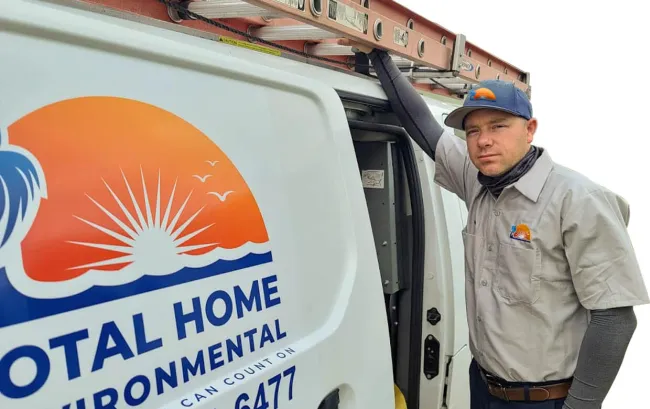 Technician leaning on a Total Home Environmental service van with company logo and ladder on top