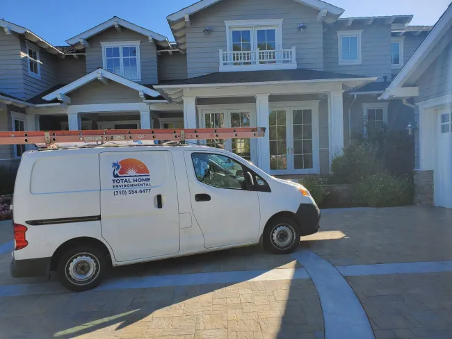 White service van with ladder parked in driveway of large gray two-story house with white trim and columns