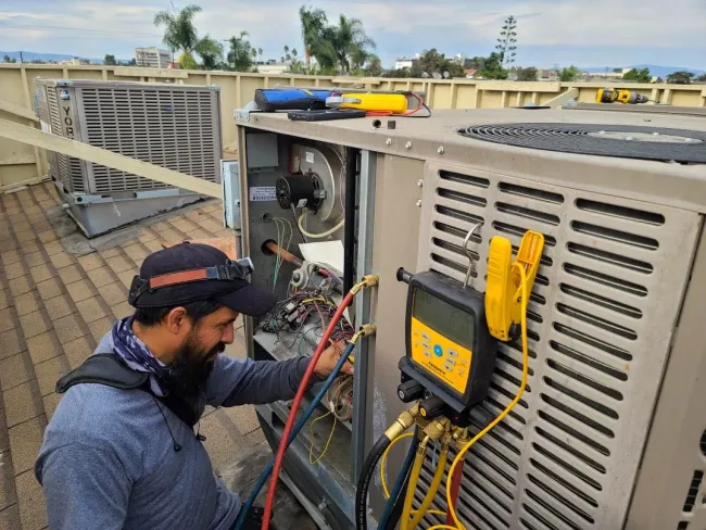 Technician inspecting and repairing rooftop HVAC unit with diagnostic tools and gauges during maintenance work.