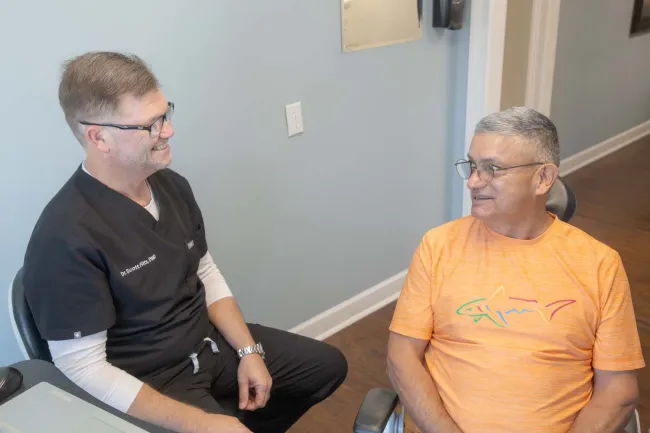 Dentist consulting with a male patient wearing an orange shark shirt in a dental office setting.