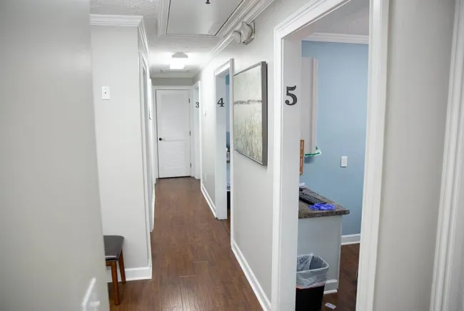 Interior hallway with wooden floors, white walls, numbered doors, and a small office room visible.