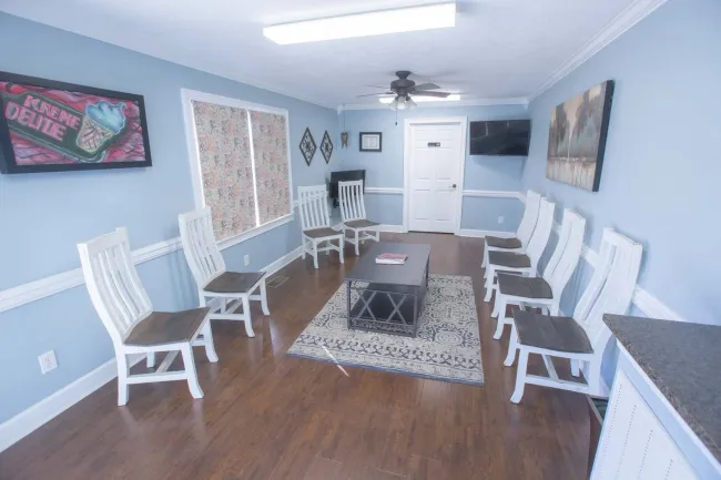 Bright waiting room with white chairs, blue walls, hardwood floor, a rug, ceiling fan, and wall art.