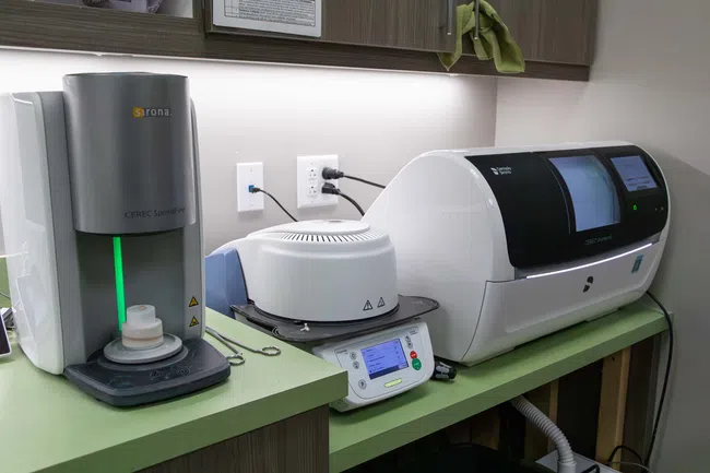 Dental CAD/CAM milling machine and equipment on green countertop in a dental office setup.