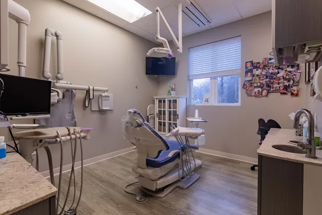 Modern dental clinic room with dental chair, equipment, TV, window, and photo collage on wall under bright lighting