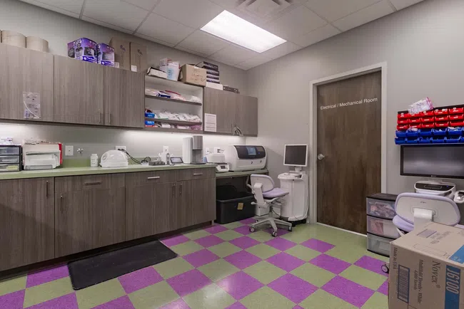 Modern medical lab room with cabinets, equipment, computer stations, and colorful green and purple tiled floor.