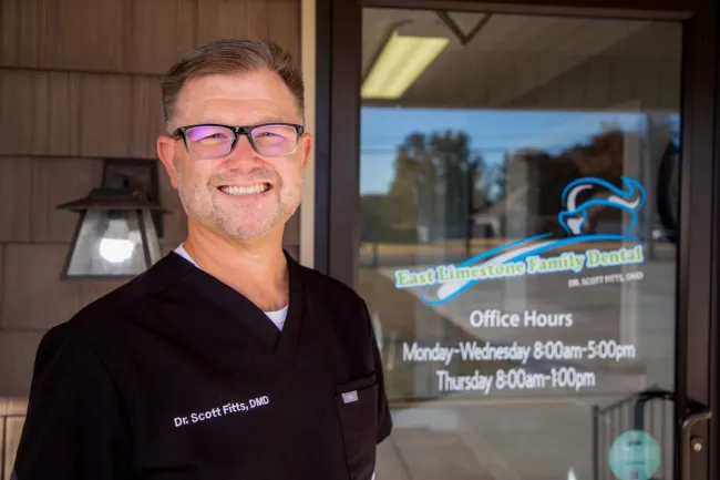 Smiling male dentist wearing glasses and black scrubs standing outside East Limestone Family Dental office.