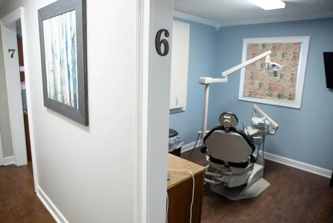 Dental clinic hallway showing room 6 with a dental chair and equipment inside a blue wall room.