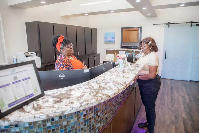Two women interacting at a front desk with granite countertop in a modern office reception area.