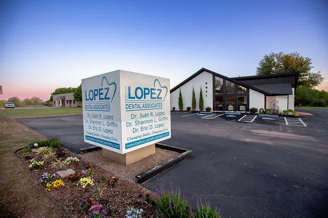 Modern dental office building with large sign for Lopez Dental Associates at dusk with clear sky.