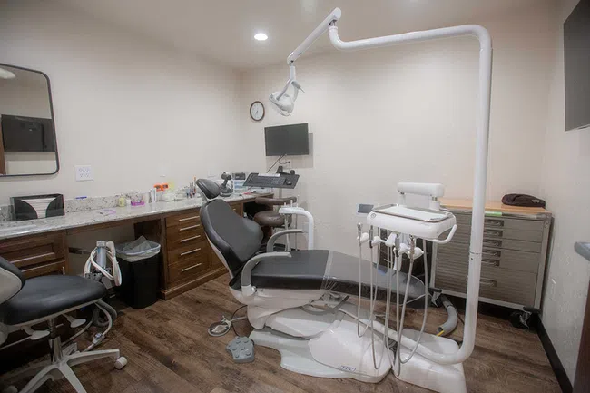 Modern dental clinic room with reclining dentist chair, equipment, monitor, and wooden cabinets on wood floor.