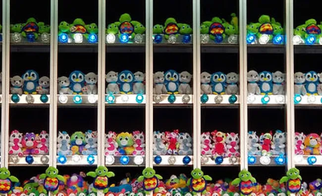 Rows of colorful stuffed animal prizes including penguins, frogs, and bears displayed behind glass panels.