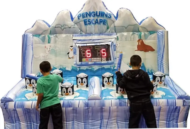 Two boys play Penguins Escape inflatable game featuring penguins, icy mountain backdrop, and digital scoreboard.