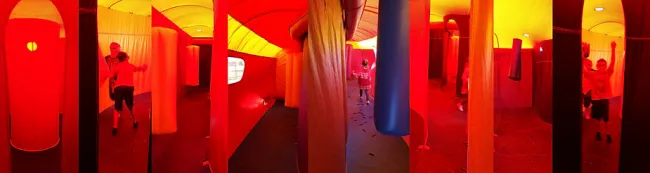 Child running and jumping inside a large red and yellow inflatable obstacle play structure.