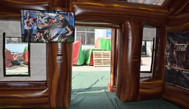 Interior view of a brown inflatable structure with a TV screen showing a race car scene and windows revealing an outdoor area.