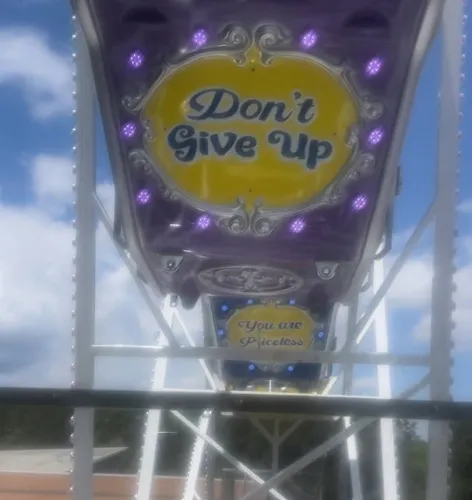Ferris wheel cabins with motivational messages Don't Give Up and You are Priceless under a blue sky.