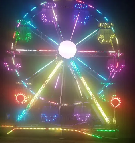 Colorful Ferris wheel lit up with vibrant LED lights against a dark night sky at a carnival.