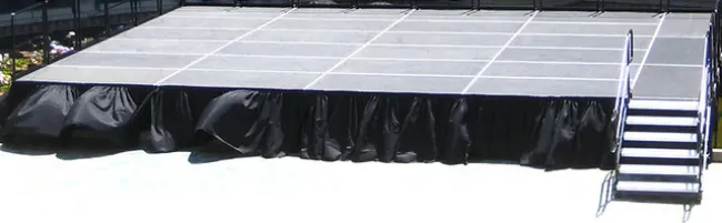 Portable stage platform with black skirting and stairs on a sunny outdoor surface.