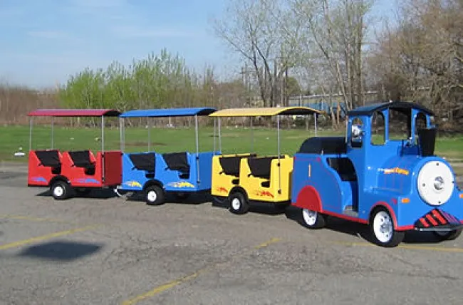 Colorful miniature train train ride for children parked outside on pavement with green grass background