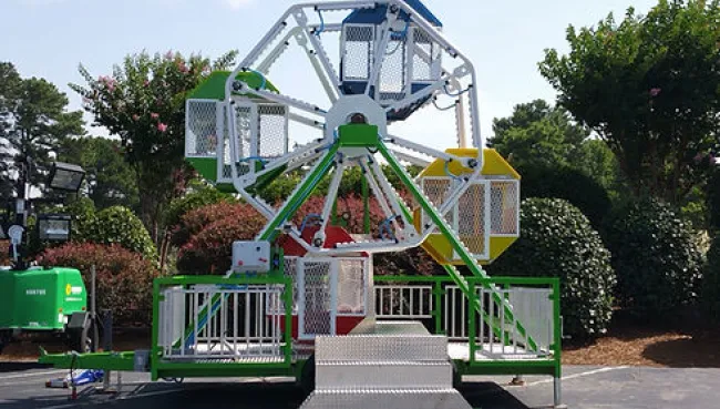Small colorful Ferris wheel ride with metal cages on a sunny day in an outdoor park setting