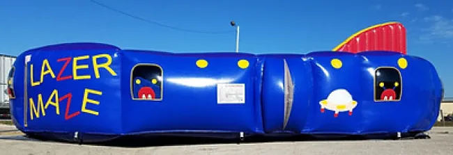 Bright blue inflatable laser maze with colorful lettering and cartoon UFO and monster designs outdoors on pavement.