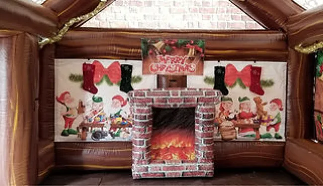 Inflatable Christmas cabin interior with a faux brick fireplace and festive decorations including stockings and elves.